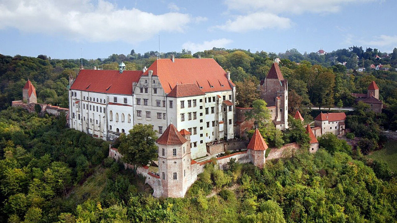 Luftbild der Burg Trausnitz in Landshut mit der historischen Schlossanlage, Wehrtürmen und den umgebenden Park- und Waldflächen.