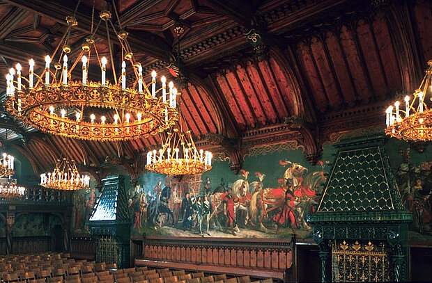 Der Prunksaal des Landshuter Rathauses mit kunstvoller Holzdecke, historischen Wandgemälden und großen Kronleuchtern.