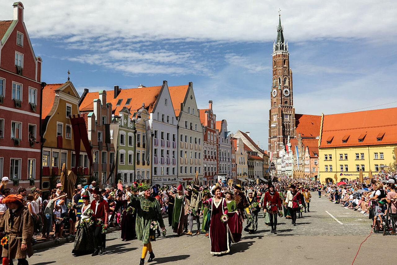 Festzug der Landshuter Hochzeit auf der Landshuter Altstadt mit historischen Kostümen und der Kirche St. Martin im Hintergrund.