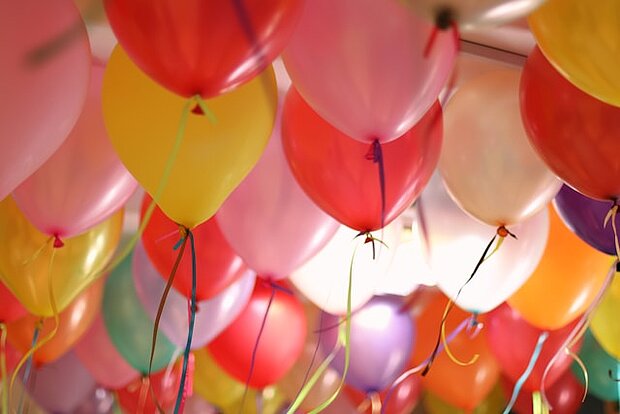 Zahlreiche farbige Luftballons mit Bändern, die dicht unter einer Decke schweben und eine festliche Dekoration bilden.