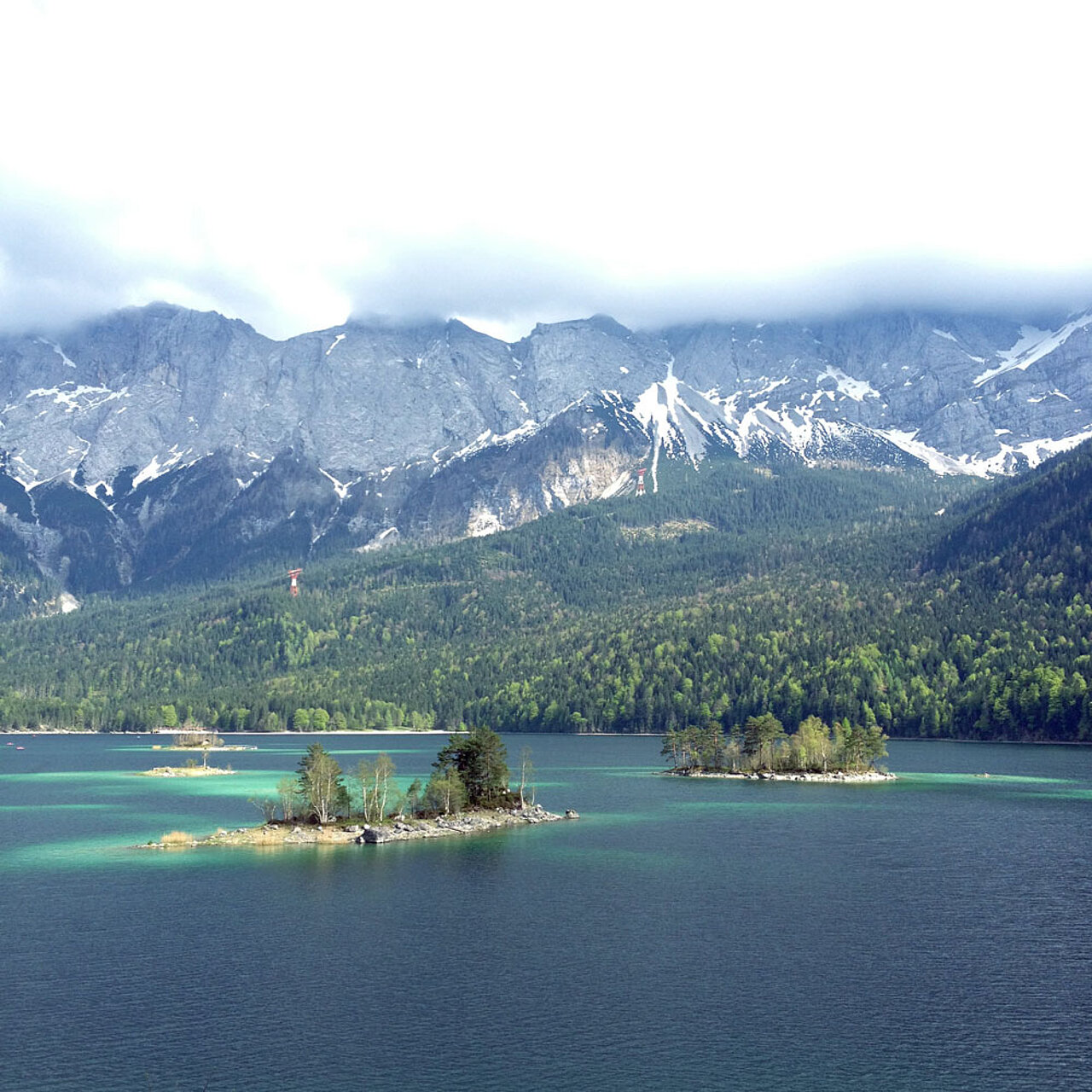 Der Eibsee mit seinen kleinen Inseln vor der Kulisse des Zugspitzmassivs und der umliegenden Alpenlandschaft.