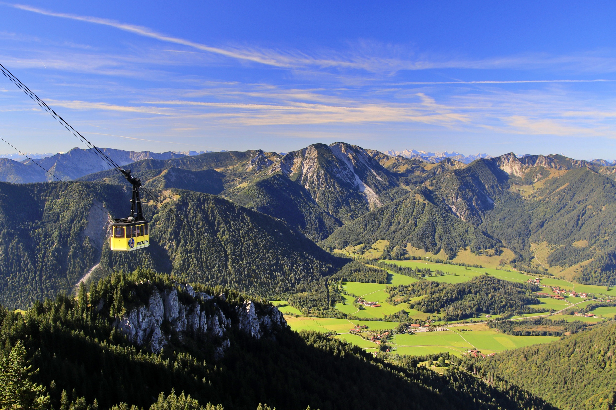 Kabine der Wendelstein-Seilbahn auf dem Weg zum Gipfel. Im Hintergrund erstrecken sich bewaldete Berge, Almflächen und das Alpenpanorama.